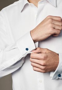 White dress shirt with a textured pattern, light blue cuff accents, and blue decorative cuff links. Button-up design with pointed collar.