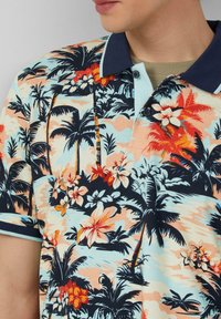 Polo à manches courtes présentant un motif tropical avec des palmiers et des fleurs dans des teintes de bleu, d'orange, de vert et de rose. Col marine en accent.
