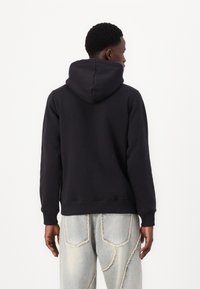 Zwarte hoodie gemaakt van zachte stof, met een grote capuchon en geribde manchetten. Gepaard met lichtblauwe jeans met contrasterende stiksels.