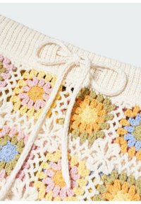 Gros plan sur une ceinture tricotée avec un cordon de serrage noué et des carrés colorés au crochet à motif floral en jaune, rose, bleu et vert.