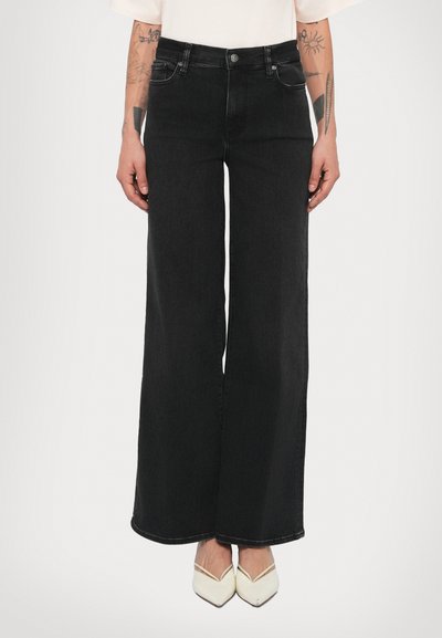Jean noir à jambes larges avec une taille haute, présentant une conception traditionnelle à cinq poches et des détails de couture subtils. Associé à des chaussures blanches à bouts pointus.