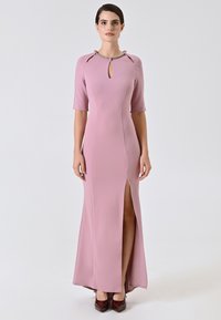 Lungo vestito rosa con maniche corte, scollatura a fessura, spacco laterale e tessuto morbido. Abbinato a décolleté bordeaux.