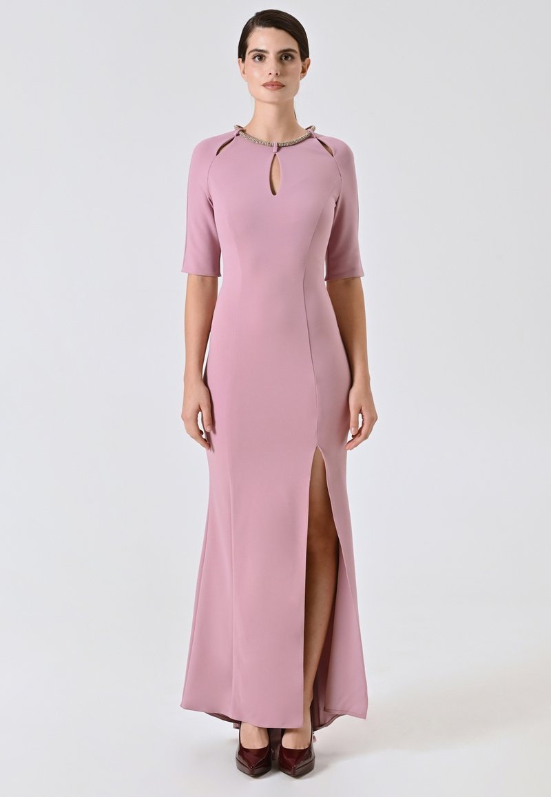 Lungo vestito rosa con maniche corte, scollatura a fessura, spacco laterale e tessuto morbido. Abbinato a décolleté bordeaux.