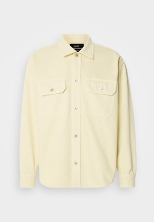 Světle žlutá, dlouhá rukávová košile vyrobená z měkké látky, s knoflíkovou přední stranou, dvěma náprsními kapsami a stříbrnými knoflíky jako dekorace.