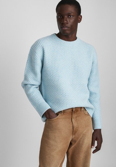 Maglione lavorato a maglia azzurro chiaro con un motivo testurizzato, collo rotondo e polsini a costine, abbinato a jeans di denim beige. Tessuto morbido e caldo.