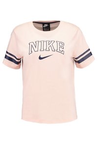 Růžové tričko s krátkým rukávem s nápisem "NIKE" v tučných námořnicky modrých písmenech, s námořnicky modrým a bílým pruhovaným vzorem na rukávech a klasickým kulatým výstřihem.