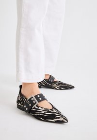 Bailarinas de punta en tela de estampado cebra en blanco y negro, con una ancha tira negra con tachuelas metálicas, usadas con pantalones cropped blancos.