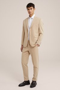 Beige puku na jaketi moja ya kifungo na suruali za mbele mbapele, ikiwa na shati la nyeupe na viatu vya loferi vyeusi. Nyenzo laini, iliyoandaliwa vizuri.