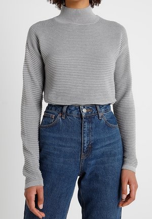 Maglione grigio a collo alto con costine e maniche lunghe, abbinato a jeans in denim blu a vita alta. Presenta un design in tessuto testurizzato.