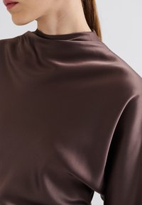 Satiini ruskea paita, jossa on korkea kaula-aukko, sileä rakenne ja rento istuvuus. Kangas näyttää pehmeältä ja siinä on hieno kiilto.