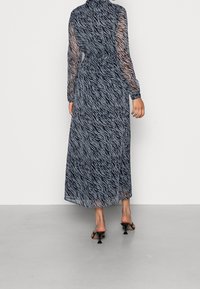 Robe maxi en tissu transparent bleu marine avec un motif zèbre, manches longues et détail à nouer à la taille, associée à des sandales à talons noires.