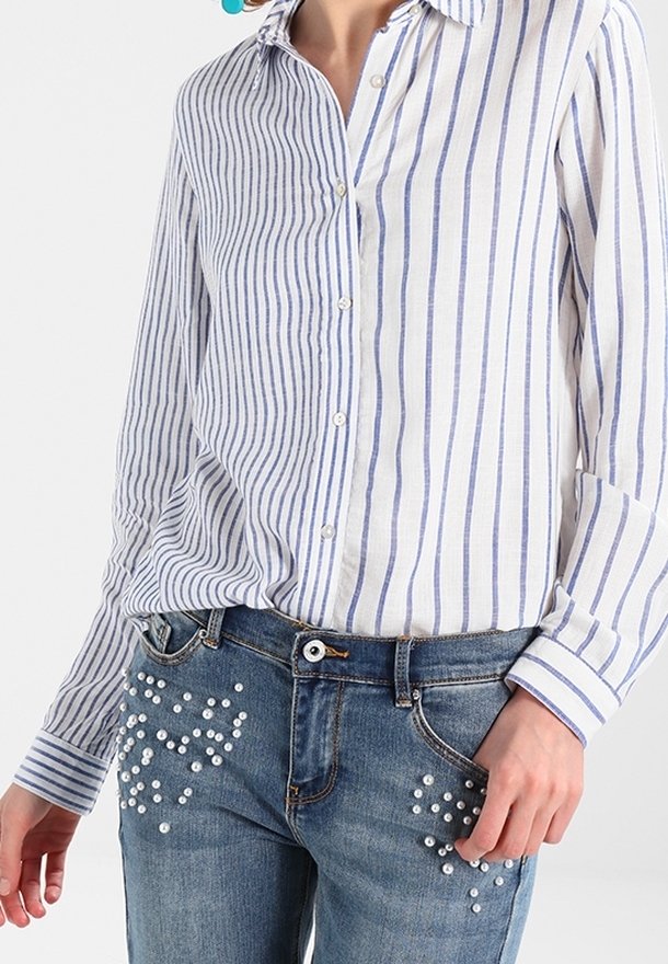 Camicia a righe bianca e blu, abbinata a jeans blu in denim con decorazioni di perle sulle tasche anteriori.