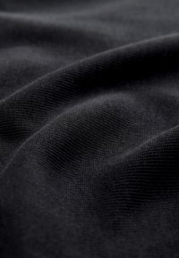 Vue rapprochée d’un tissu noir montrant une texture fine tricotée et des plis doux avec des variations subtiles de lumière et d’ombre.
