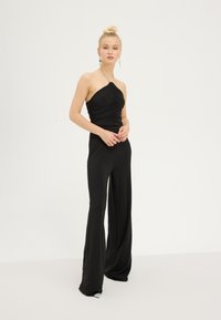 Crni kombinezon s prilagođenim korzetom koji ima nabore i halter izrez. Šire nogavice i glatka tkanina čine elegantnu siluetu.