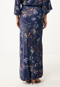 Lange, marineblauwe bloemenjurk met een zachte textuur, uitgerust met witte en bruine bloemmotieven, gecombineerd met beige hakken en vloeiende mouwen.