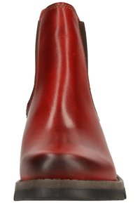 Červená kožená kotníková obuv s hladkým povrchem, elastickými bočními panely a zaoblenou špicí. Pevná černá gumová podešev s texturovaným vzorkem.