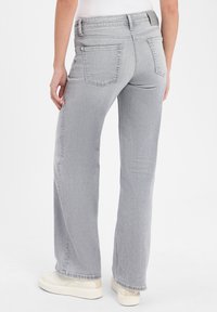 Jeans in denim grigio con design a gamba dritta, cinque tasche e vita media. Il tessuto ha una texture liscia e dettagli sbiaditi sottili.