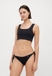Black bikini set featuring a square-neck crop top and adjustable tie-side bottoms. Made of smooth material with a subtle logo detail.