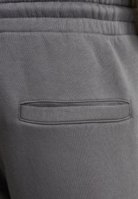 Grå sweatpants med et blødt, tekstureret stof, en elastisk talje og en lille, diskret baglomme med en vandret åbning.
