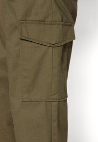 Olivegrüne Cargo-Hose aus einem strukturierten Stoff, mit einer großen Seitentasche mit Klappe und verstärkten Nähten für besondere Langlebigkeit.