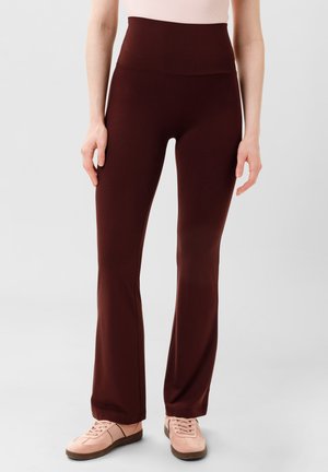 Bordeaux hoge taille flare broek, gemaakt van rekbaar materiaal met een gladde textuur. Gecombineerd met lichtroze sneakers.