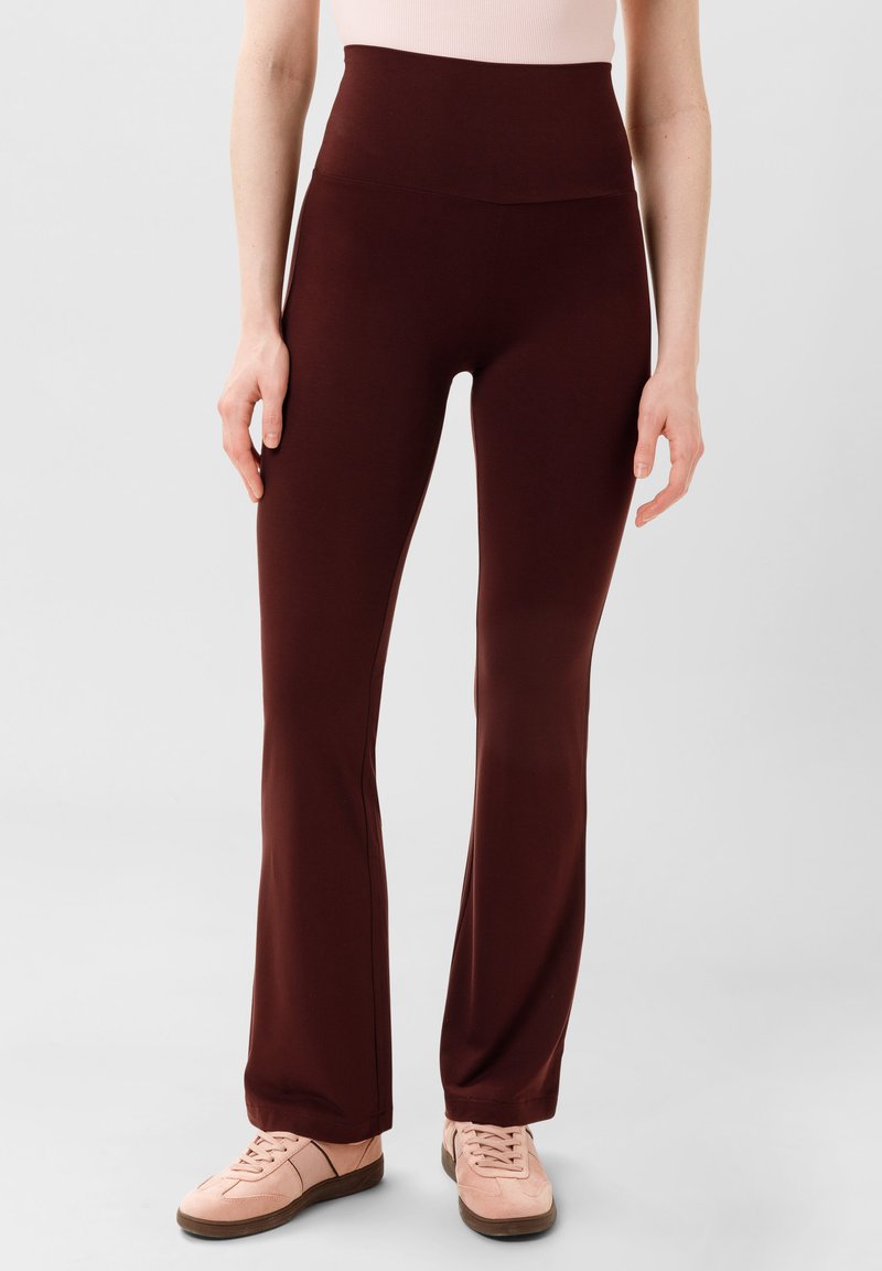Bordeaux hoge taille flare broek, gemaakt van rekbaar materiaal met een gladde textuur. Gecombineerd met lichtroze sneakers.