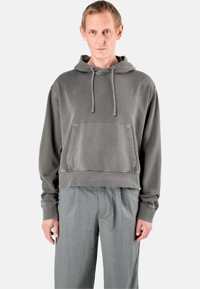 Grijze cropped hoodie met koordjes en een zak aan de voorkant, gemaakt van een gestructureerde stof. Gecombineerd met lichtgrijze losvallende broeken.