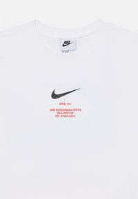 White Nike t-shirt featuring a black swoosh logo and red text with address details. Cotton material with a crew neck design.