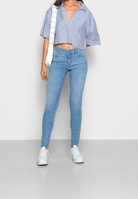 Camisa corta a rayas azul y blanca con cuello, combinada con jeans ajustados azul claro y zapatillas blancas. Diseño simple y estilo casual.