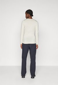 Haut crème léger à manches longues avec une texture lisse, associé à un pantalon droit noir. Design simple, sans motifs ni accents visibles.