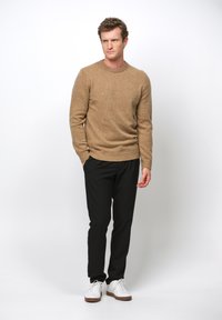 Bruine gestructureerde trui, zwarte tapered broek en witte sneakers met bruine zolen. Eenvoudig ontwerp, aansluitende snit en relaxte pasvorm.