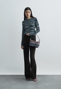 Gebreide gestreepte top met lange mouwen in tinten blauw, gecombineerd met bruine, patroonvolle uitlopende broek en een kleine meerkleurige zigzagtas.