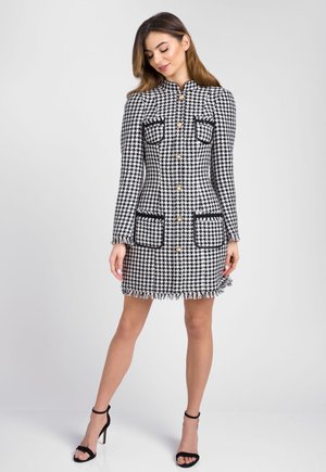 Czarna i biała sukienka w wzór houndstooth o dopasowanej sylwetce, złotych guzikach, dwóch przednich kieszeniach oraz frędzlach na dole.