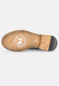 Schwarze Schuhsohle aus strukturiertem Korkmaterial, mit mehrfarbigen Sprenkeln, einem kreisförmigen Logostempel und einem glatten schwarzen Absatzbereich.