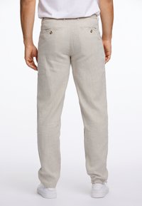 Lichtbeige linnen broek met een relaxte pasvorm, voorzien van twee achterzakken met knoopsluitingen en rechte pijpen, gecombineerd met witte sneakers.