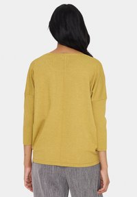 Haut tricoté jaune à coupe décontractée, manches trois-quarts et détail de couture centrale. Texture douce et encolure arrondie.