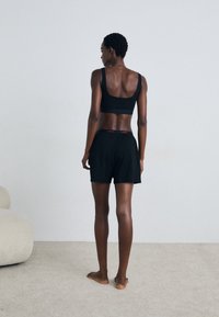 Svart sports-bh med brede stropper og scoop-back; kombinert med løse svarte shorts med et rødt midjebånd.