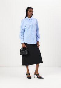 Light blue button-down shirt with white stripes, paired with a black midi skirt. Accessories include a black handbag and black heels with buckle details.