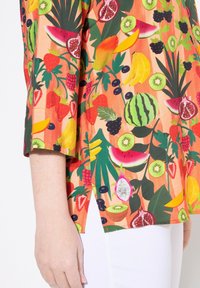 Top a maniche corte con motivo di frutta, caratterizzato da colori vivaci come arancione, verde e rosa, con una vestibilità comoda e spacchi laterali per un tocco aggiuntivo.