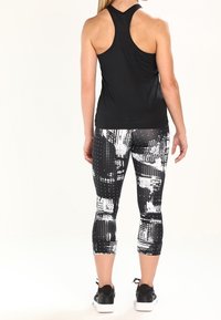 Černý sportovní tílko s designem na zádech, v kombinaci s capri legínami s černobílým abstraktním vzorem, obuté s černými teniskami.