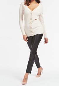 Cardigan beige a costine con scollatura a V profonda e bottoni anteriori, abbinato a legging in ecopelle neri e tacchi alti color nudo.