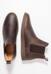 Botas de tobillo de cuero marrón con un acabado texturizado, paneles laterales elásticos y una lengüeta en el talón. Suela de goma plana con detalle de costura.