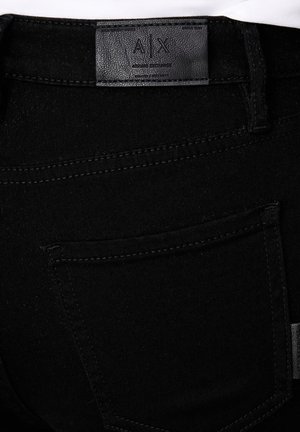 Vaqueros negros de mezclilla que muestran el bolsillo trasero y la etiqueta de cuero A|X Armani Exchange en la cintura.
