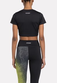 Melnā sporta krekls ar īsām piedurknēm, apvienots ar melnajām legingām ar gradientu, kas pāriet no pelēkas uz laima zaļu. Redzams Reebok zīmols.