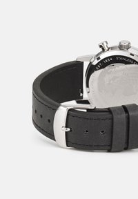 Black leather watch strap with silver stainless steel clasp and case, featuring an engraved back with a globe design.