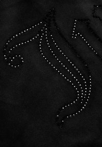 Černá látka se zakřivenými a přímými liniemi vytvořenými malými lesklými černými a stříbrnými kamínky uspořádanými v dekorativním vzoru.