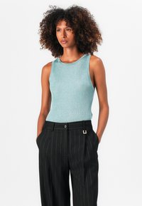 Débardeur sans manches bleu clair à côtes associé à un pantalon noir à rayures, avec un accent doré à la taille.