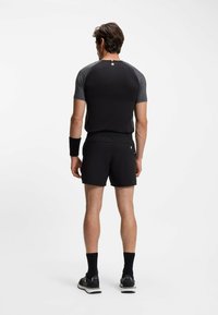 Heren sportoutfit met een zwart T-shirt met korte mouwen en grijze accenten, en zwarte shorts. Een zwart polsbandje en sneakers maken de look compleet.