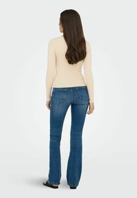 Beige ribbed lange mouw top gecombineerd met blauwe flared jeans, die een getailleerde silhouet en een soepele stofstructuur toont.
