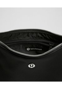 Czarna torba sportowa z srebrnym zamkiem, gładka tkanina i metka z logo w środku. Posiada kieszeń na zamek błyskawiczny i minimalistyczny design.